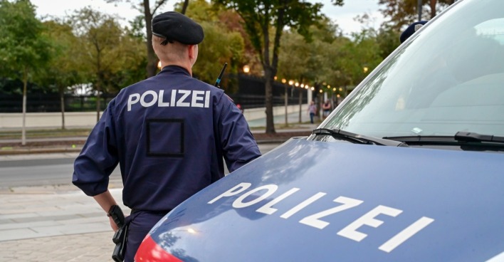 Polizist mit dem Polizeiwagen. Polizist in einheitlicher Patrouille auf der Straße. Polizeisymbol am Fahrzeug und Uniform für die Bluttat in Kärnten.