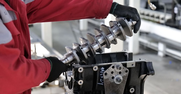 Mitarbeiter montiert eine Kurbelwelle in einem Motorblock in einem Volkswagen-Werk – Symbolbild für Stellenabbau, Konzernumbau und die Transformation der Automobilindustrie.