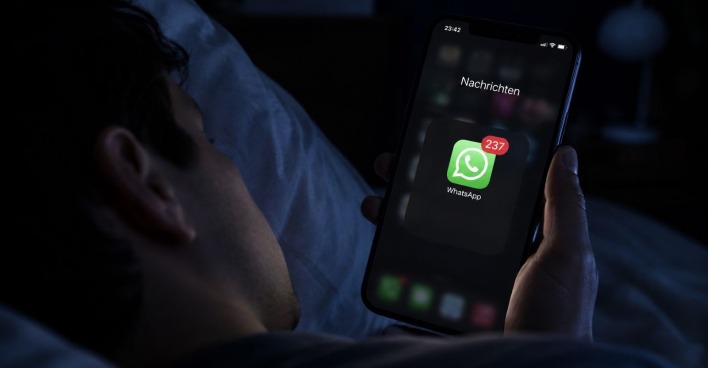 Mann liegt mit Handy im Bett, am Display WhatsApp-Nachrichten