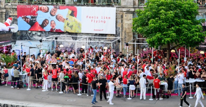 Menschenmenge beim Public Viewing am Donaukanal in Wien während eines Fußballspiels, viele Fans in rot-weiß gekleidet, Szene vor der Eskalation der Gewalt