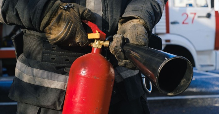 Symbolbild: Feuerwehr mit Feuerlöscher bei einem Einsatz nach einem E-Auto-Brand infolge eines Verkehrsunfalls.