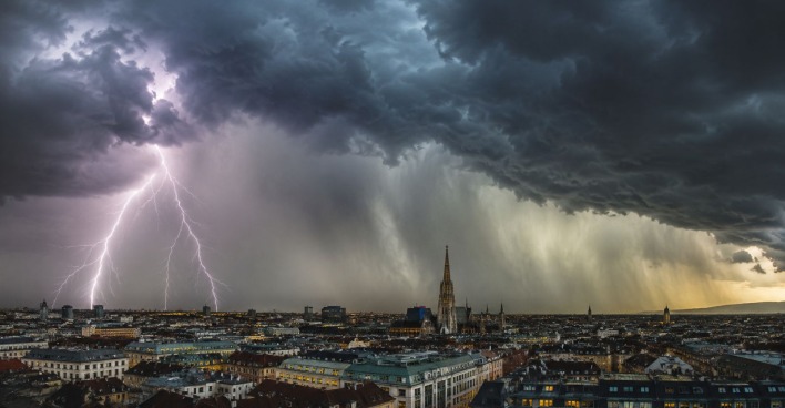 Gewitterfront mit Blitz, Starkregen und dunklen Wolken über einer Stadt in Österreich, Unwetter mit Hagel und Sturm zieht auf