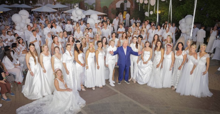 Robert Rogner in einem blauen Anzug, umringt von Frauen in weißen Brautkleidern