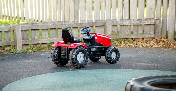 Ein roter Kinder-Trettraktor steht im Freien