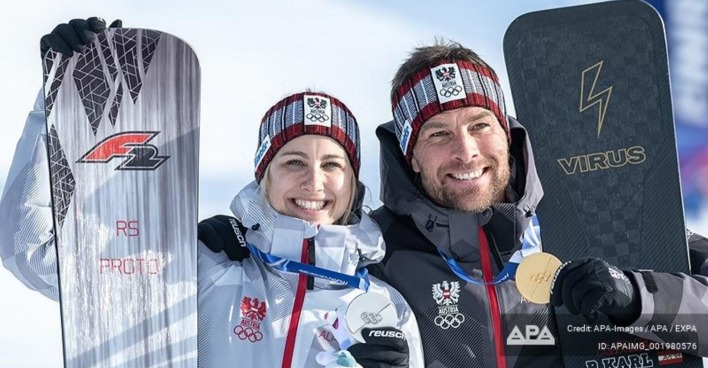 Sabine Payer strahlt gemeinsam mit ihrem Ehemann Alexander Payer nach einem erfolgreichen Wettkampf im österreichischen Nationalteam mit Snowboards und Olympia-Medaille.