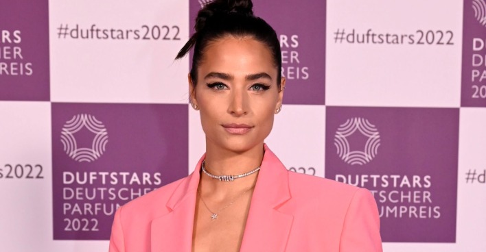 Amira Aly bei einer Veranstaltung im pinkfarbenen Blazer vor einer Fotowand.