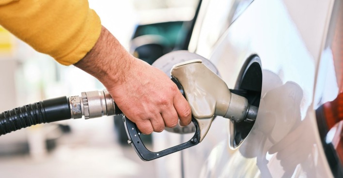 Hand eines Autofahrers mit gelbem Pullover beim Tanken eines weißen Autos