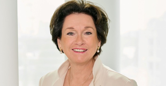 Frau mit Perlenohrringen und in beiger Jacke