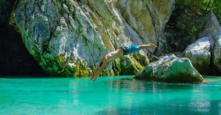 Mann springt in die türkisfarbene Soča zwischen Felsen in Slowenien.