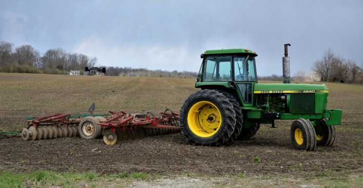 Grüner Traktor mit gelben Rädern und angehängtem Ackergerät auf einem Feld./ Ein 12-jähriger Bub ist bei einem Traktorunfall in Bünde verunglückt