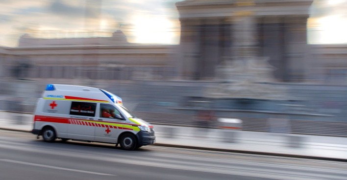 Rettungsauto fährt auf einer Straße, dahinter ist ein Gebäude zu sehen
