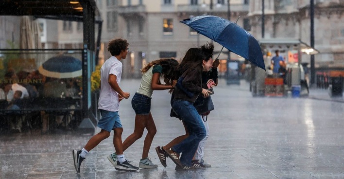 Menschen laufen bei Starkregen mit einem Regenschirm durch eine italienische Stadt.