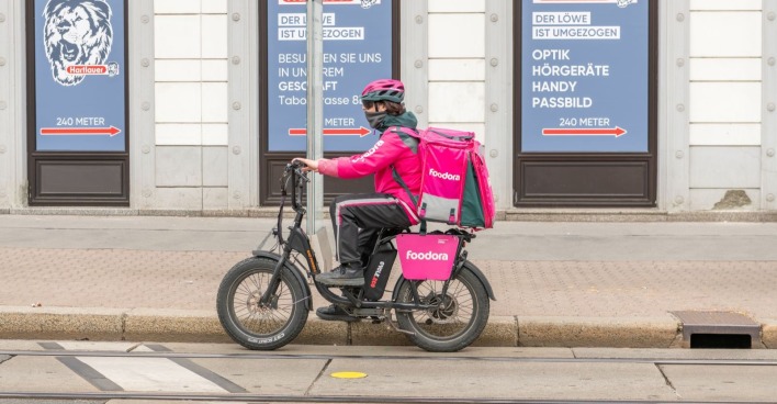 Foodora-Zusteller fährt nach E-Moped-Änderung mit einem E-Bike durch Wien.