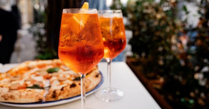 Gläser gefüllt mit Aperol auf einem Tisch mit Pizza