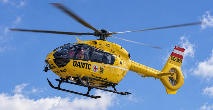 Gelber ÖAMTC-Rettungshubschrauber fliegt vor blauem Himmel mit weißen Wolken.