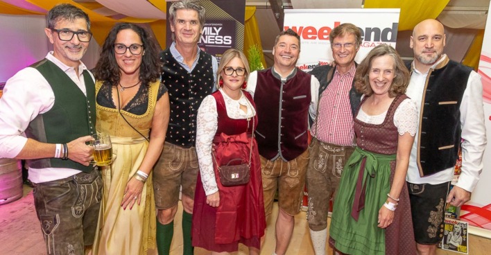 Acht Personen in Tracht vor Werbebannern im Festzelt