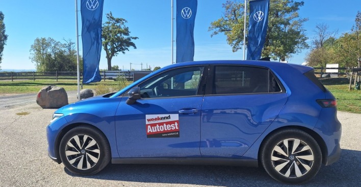 Ein blauer ID Polo parkt in der Sonne. Im Hintergrund sind blaue VW-Fahnen zu sehen und eine grüne Wiese.