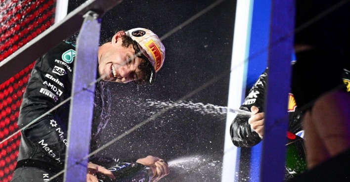 Kimi Antonelli im schwarzen Mercedes-Rennanzug und mit Pirelli-Kappe spritzt bei einer Formel-1-Siegerehrung lachend Champagner.