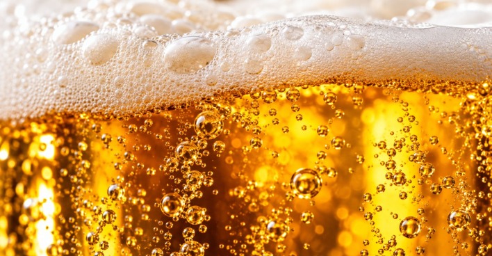 Makroaufnahme von goldgelbem Bier mit weißer Schaumkrone und aufsteigenden Kohlensäurebläschen.
