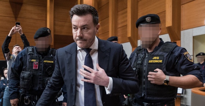 René Benko im Anzug zwischen Justizwachebeamten bei einem Gerichtstermin. Das Landesgericht Innsbruck hat dem früheren Signa-Chef eine Fußfessel bewilligt.