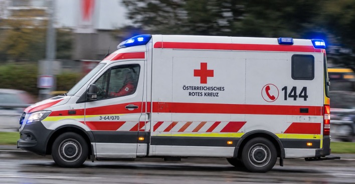 Rettungswagen des Österreichischen Roten Kreuzes mit eingeschaltetem Blaulicht, seitlich auf einer Straße aufgenommen, KI-Themenbild.