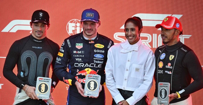 Max Verstappen mit Siegerpokal beim Singapur Sprint 2026, gemeinsam mit Charles Leclerc und Lewis Hamilton bei der Siegerehrung.