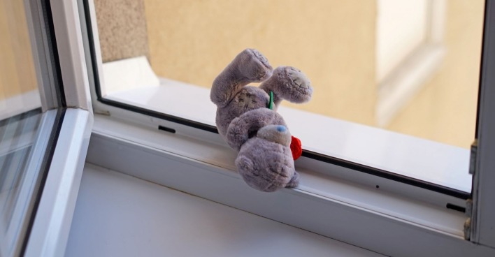 Ein kleiner Teddybär vor einem offenen Fenster.