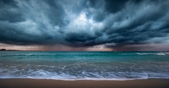 Dunkle Gewitterwolken über dem Meer mit Wellen am Strand als Symbolbild für die Unwetterwarnung in Italien