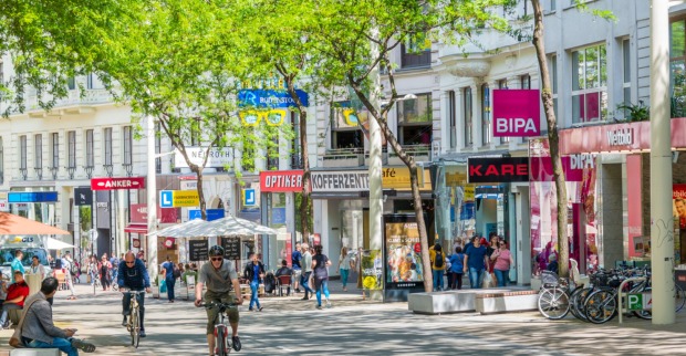 Radfahrer und Passanten auf einer belebten Einkaufsstraße, verschiedene Shops