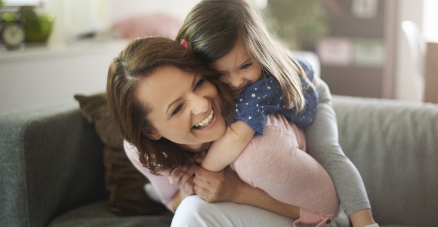 Ein kleines Mädchen umarmt von hinten eine lachende junge Frau | Credit: iStock.com/gpointstudio