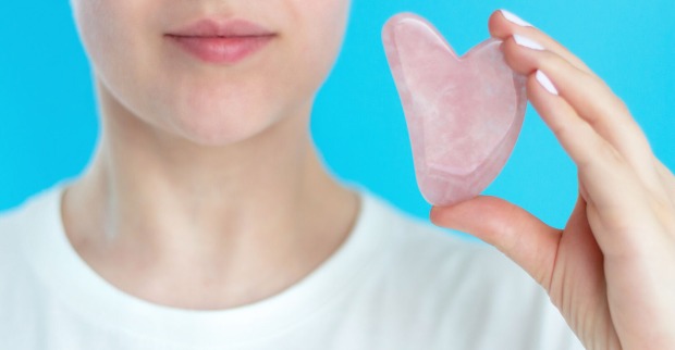 Frau hält Stein zur Gua-Sha Massage hoch