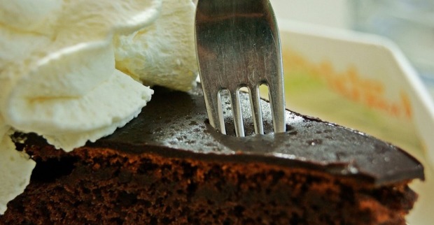 Eine Gabel sticht in eine Sacher-Torte mit Schlagobers