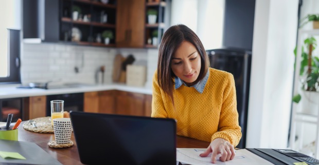 Eine Frau arbeitet auf ihrem Küchentisch vor ihrem Laptop