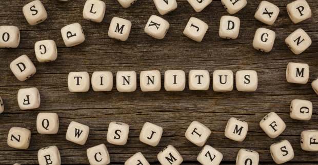 Mehrere Buchstabenwürfel bilden auf einem Holztisch das Wort Tinnitus