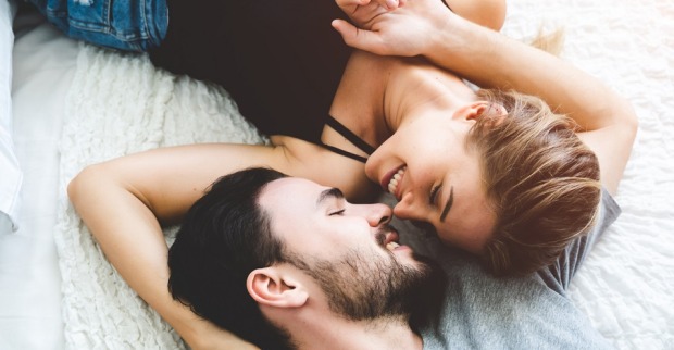 Ein junges Pärchen liegt am Bett und küsst sich.