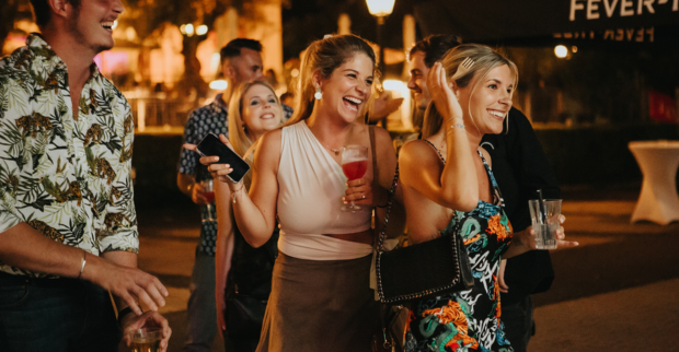Nacht, zwei Frauen die lachen und Drinks in der Hand halten.