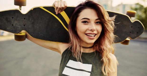 Junges Mädchen mit ihrem Skateboard hinter dem Körper verschränkt | Credit: iStock.com/diignat