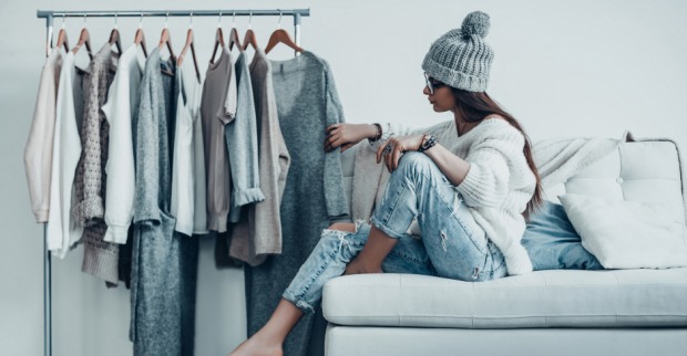 Junge Frau sitzt vor dem Kleiderständer und durchforstet ihre Garderobe | Credit: iStock.com/g-stockstudio