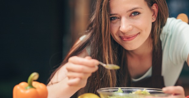 Eine junge Frau mit langen, braunen Haaren schmeckt zufrieden ihr Essen ab | Credit: iStock.com/Deklofenak