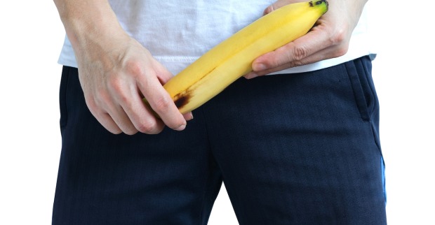 Ein Mann in Jeans hält sich eine nach oben weisende  Banane vor den Schritt