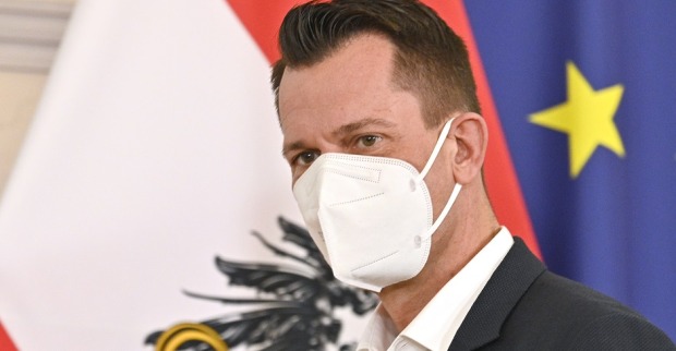 Gesundheitsminister Wolfgang Mückstein mit FFP-2 Maske vor der europäischen und österreichischen Flagge.