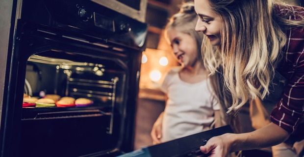Junge Mutter öffnet Backrohr, um nach den Muffins zu sehen | Credit: iStock.com/Vasyl Dolmatov