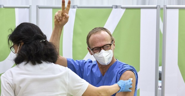 Virologe Christoph Wenisch erhält eine Impfung und zeigt mit den Fingern glücklich das Victory-Zeichen