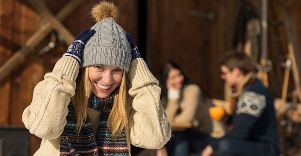 Junge fröhliche Frau vor einer Almhütte bei winterlichen Temperaturen | Credit: iStock.com/CandyBoxImages