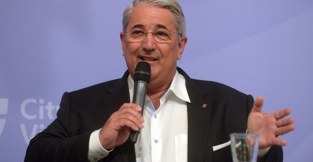 Bezirksvorsteher Ernst Nevrivy vor der Pressewand der Stadt Wien. Er hält ein Mikrofon in der Hand und spricht