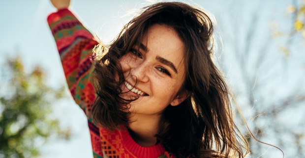 Junge fröhliche Frau beim Spazierengehen an einem sonnigen Herbstnachmittag | Credit: iStock.com/Yuricazac