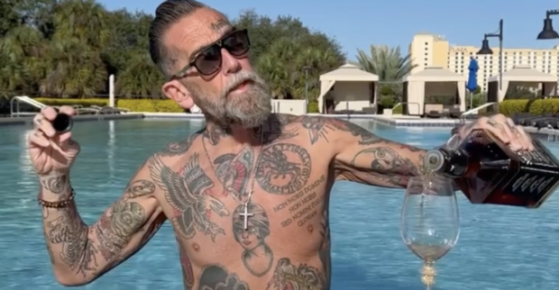 Roland Ludomirska mit nackten Oberkörper, voll tättowiert und einer Flasche Jack Daniels in einem Pool