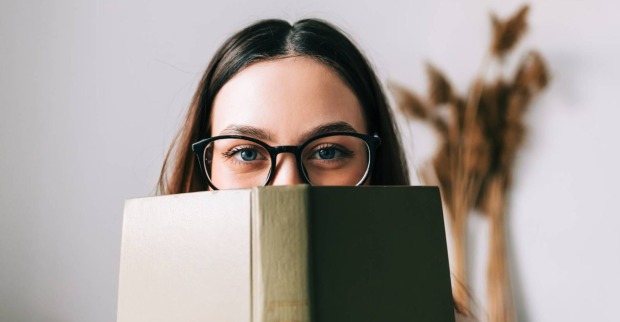Junge Studentin verbirgt ihr Gesicht hinter einem Buch | Credit: iStock.com/nikkimeel