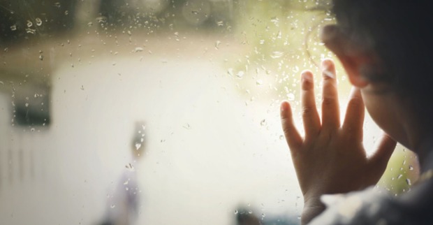 Kind hat Hand am Fenster und schaut raus