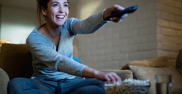 Frau schaltet mit Fernbedienung Fernseher ein